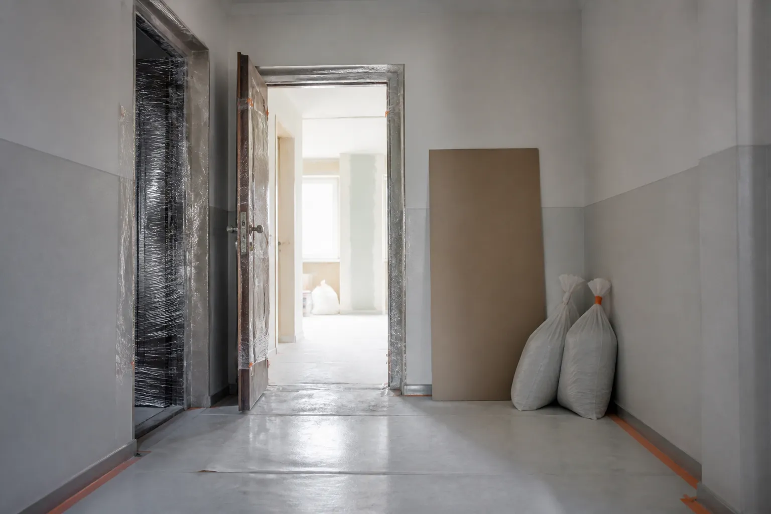 Palier d’un seul étage protégé par un film au sol et des protections sur les huisseries, devant une porte palière ouverte sur un logement en travaux