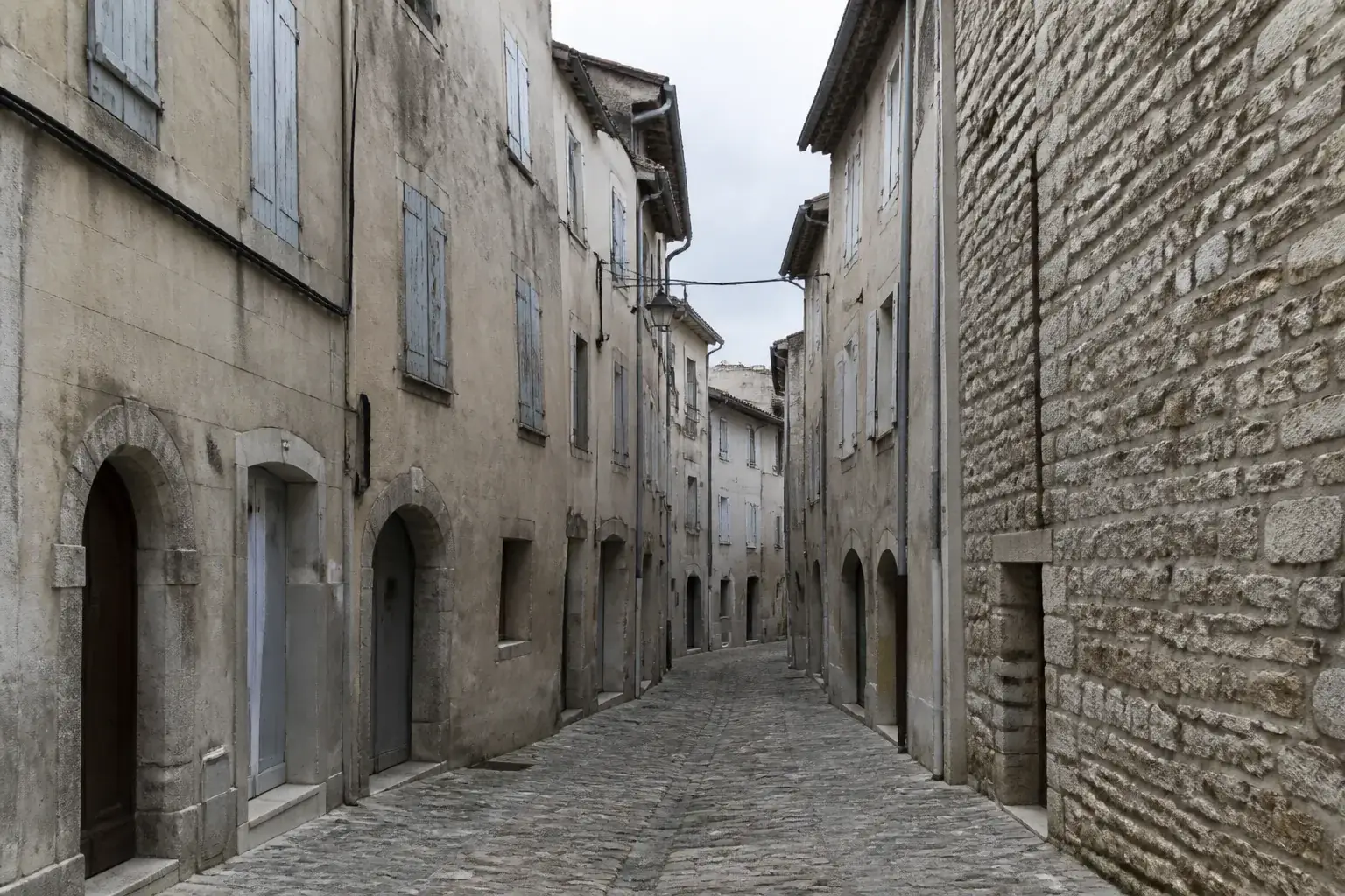 Ruelle étroite d’un vieux bourg perché, maisons hautes mitoyennes aux enduits patinés, linteaux de pierre au-dessus des ouvertures