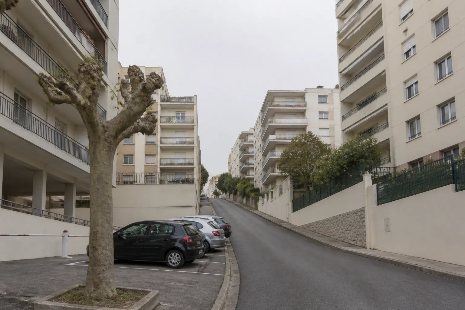 Rue résidentielle en pente bordée d’immeubles d’habitation de quatre à huit étages des années 1960 et 1970, enduits clairs et balcons filants