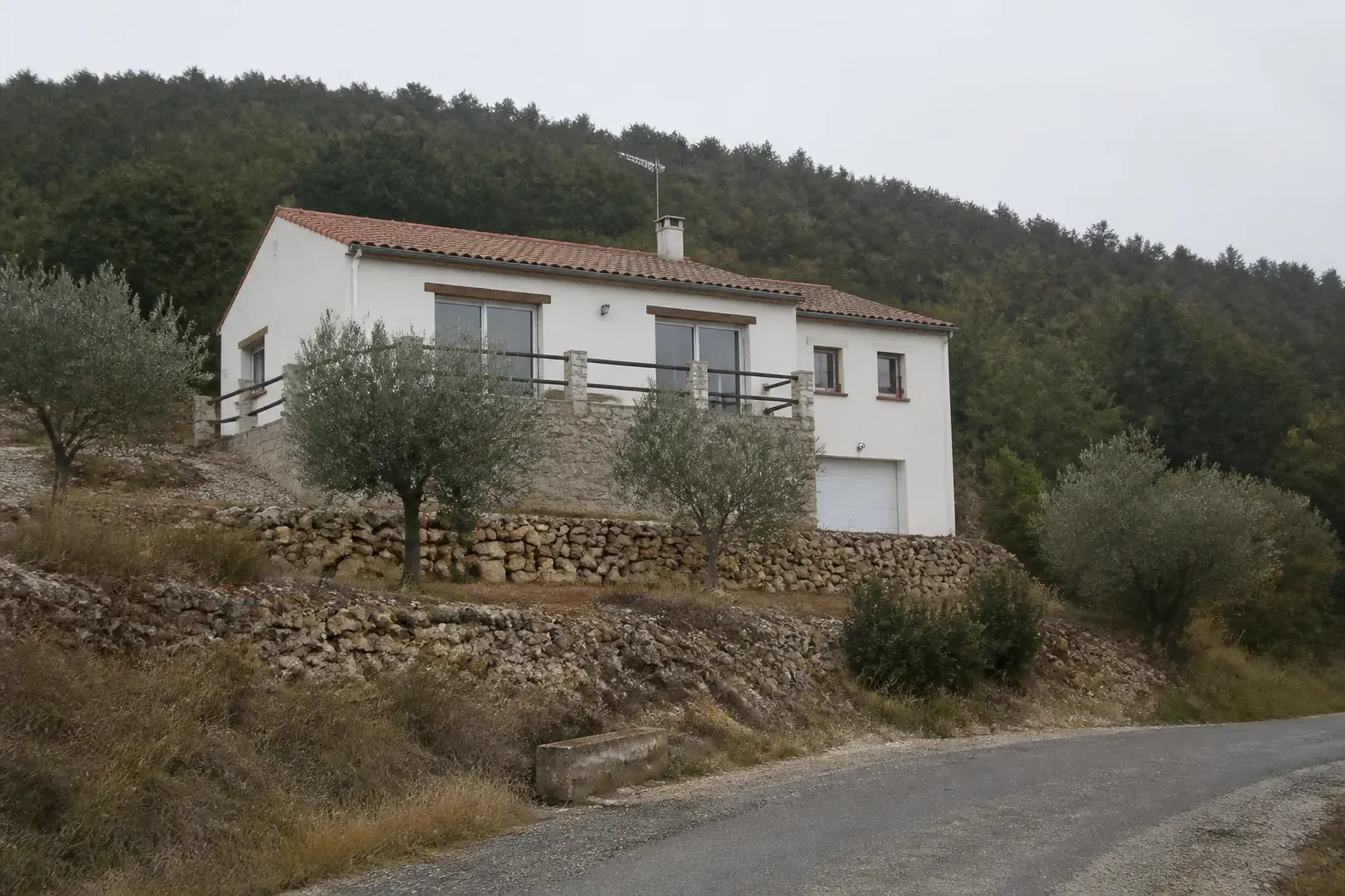 Maison individuelle bâtie à flanc de coteau, volume simple à toiture de tuiles, terrasse sur muret et restanques en contrebas